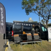 黑色 Sunlight露營車於戶外市集活動現場展示，車側設置座椅與品牌旗幟，呈現露營車生活情境體驗