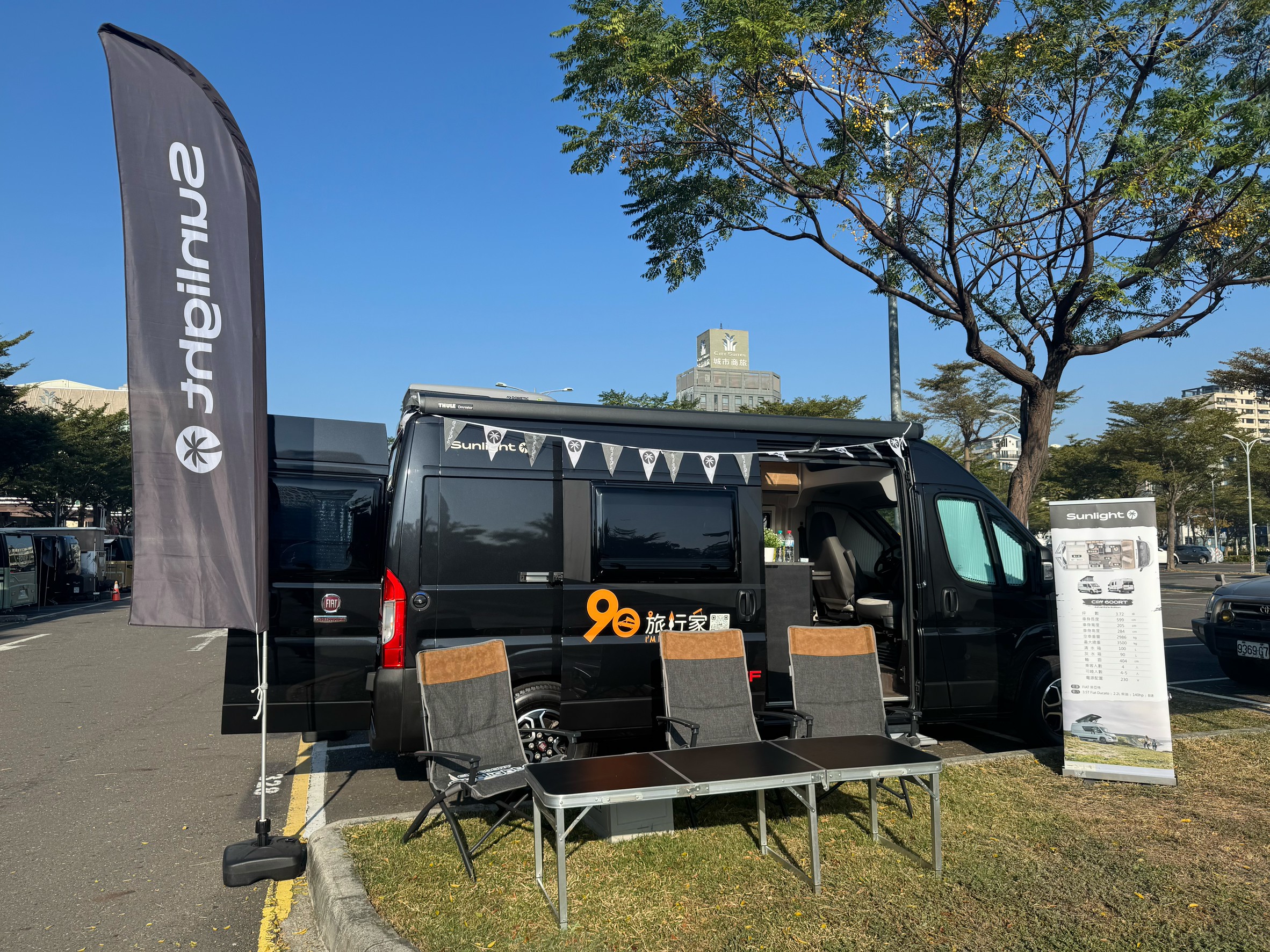 黑色 Sunlight露營車於戶外市集活動現場展示，車側設置座椅與品牌旗幟，呈現露營車生活情境體驗