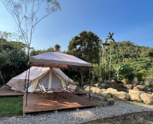 山林環繞的寵物友善露營區，木棧板上設有白色帳篷與遮陽棚，配置戶外桌椅，環境寬敞安靜，適合親子與寵物一同露營體驗