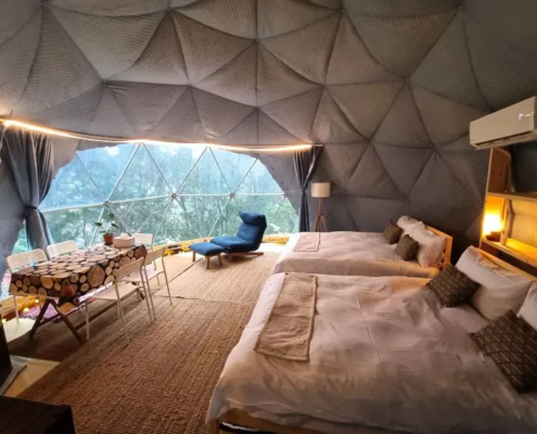 寵物友善露營區的帳篷內部空間，設有雙人床、簡約家具與室內燈光，帳篷前方可欣賞自然綠意景觀，提供舒適安靜的露營住宿體驗