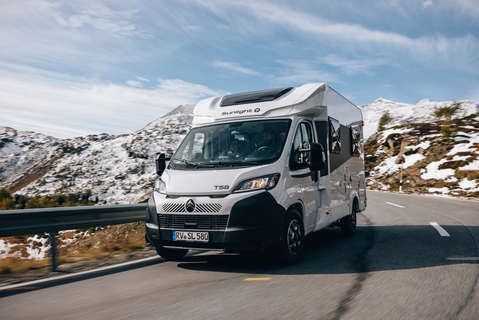 白色 Sunlight T58 行駛於高山道路，周圍是雪山與開闊自然景觀，呈現露營旅行的自由感