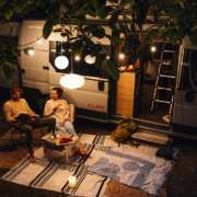 Sunlight Cliff 露營車停在戶外營地，兩人在車外燈串與露營燈下休息聊天，展現露營車旅行與數位游牧生活情境